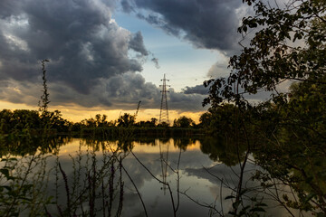 Fototapeta na wymiar Wonderful sunset with approaching storm clouds over Savica fishing pond on the outskirts of Zagreb city, Croatia and electric pole reflected in the water surface