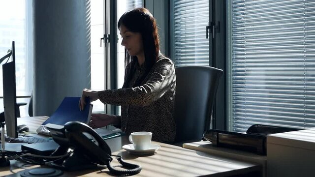 Young female worker in industrial espionage concept. The secretary puts coffee on the table in the office and looks for the necessary documents, and then photographs them
