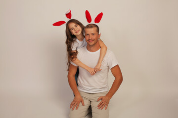 a young happy guy in a white T-shirt hugs his daughter in a white T-shirt on her head bunny ears easter