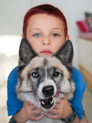 A boy with heterochromia hugs a mongrel beautiful domestic dog. Child and pet, close-up portrait,...