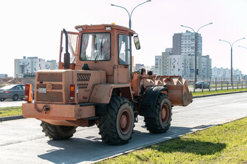 A wheeled bulldozer with a bucket is conducting road construction work in the city.