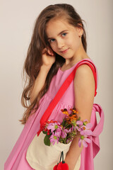 a girl with long hair in a pink linen dress with a bag on her shoulder with flowers