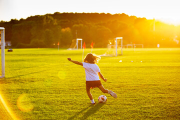 Young girl kicking a soccer ball at sunset on the soccer field 