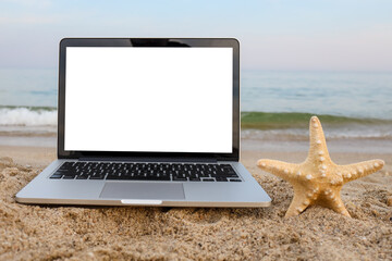 Laptop and starfish on the sand on the beach in summer in the background with a white screen.