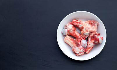 Raw pork bones in white bowl on dark background.