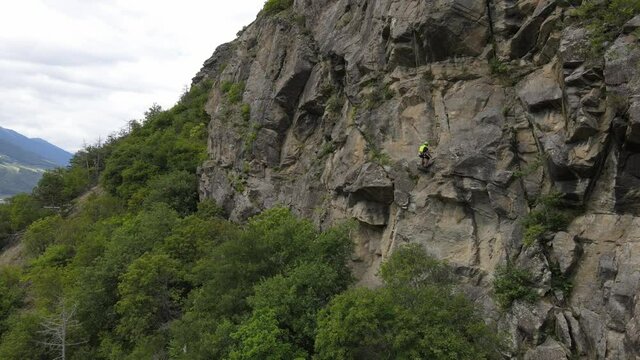 Strong muscular man rock climber, rappels down and removes the quickdraw on the hooks. successful completion of the climbing route. Outdoor rock climbing and active lifestyle concept, drone shot