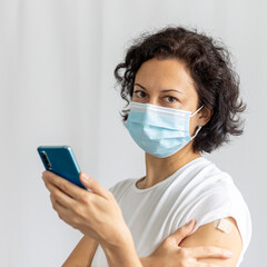 young woman in mask with plaster on her shoulder, after vaccination, young person using a mobile phone