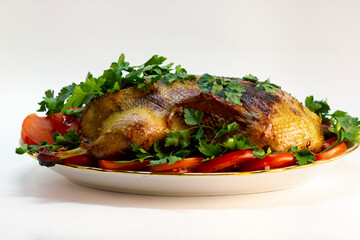 festive dish baked duck with a crispy crust garnished with slices of tomatoes and herbs on a large plate close-up on a white background