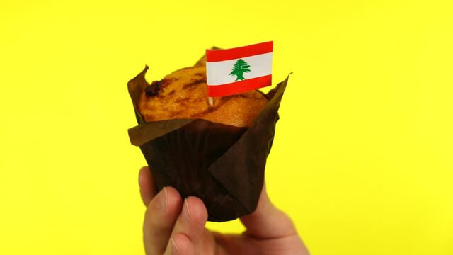 Cupcake with Lebanese flag on male palm against yellow background