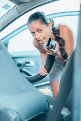 Chica joven feliz bromeando con la aspiradora mientras limpia su vehículo en el túnel de lavado de coches