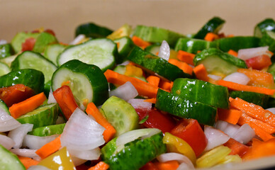 Salad of fresh vegetables in close-up. Cucumbers, carrots, tomatoes, peppers, onions are chopped and mixed