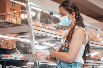 Consumidor con mascarilla y cumpliendo la distancia de seguridad eligiendo un artículo de ...