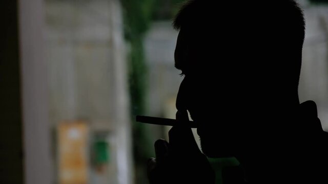 Silhouette of a man smoking a cigarette outdoors evening time close up