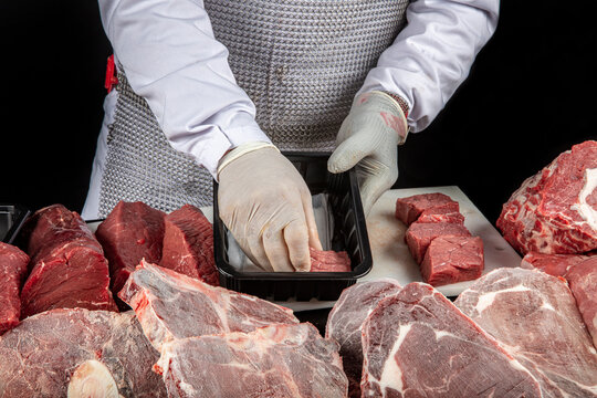 Butcher cutting beef. Chef in white latex gloves holding pieces of raw beef on a white polyurethane cutting board, on a dark background.