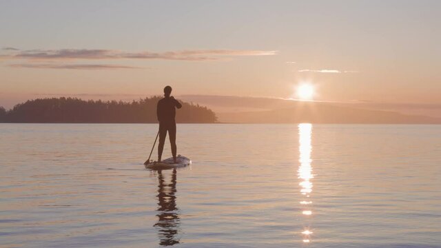 Adventurous Caucasian Adult Woman on a Stand Up Paddle Board is paddling on the West Coast of Pacific Ocean. Sunny Sunrise. Victoria, Vancouver Island, BC, Canada. Slow Motion