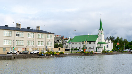 Beautiful view of the Iceland Church with white walls and green roof in front of the lake on a cloudy sky in Reykjavik, Iceland. Architecture, landmark, worship service, religion, faith concept