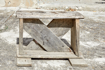 Very old wooden stool, in a concrete paved courtyard.