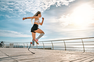 No limits. Active disabled woman with leg prosthesis in sports clothing jumping while her morning...