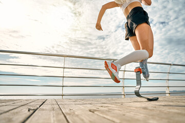 Cropped photo of a young woman with a prosthetic leg running on the bridge. Female sportsperson training outdoors.