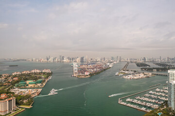 Incredible aerial view over the Miami shipping channels with the skyline on the horizon beyond and cloudy sky above as boats and ferries make their way to and from Fisher Island below.