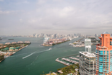 Incredible aerial view over the Miami shipping channels with the skyline on the horizon beyond and cloudy sky above as boats and ferries make their way to and from Fisher Island below.