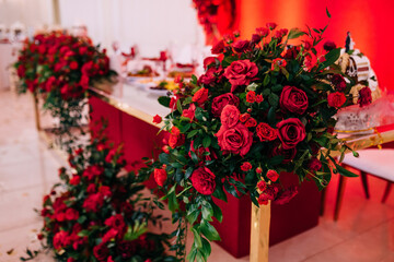 Wedding decoration of the hall. Red and white tablecloths, beautiful decor and dishes, fresh flowers on the table.
