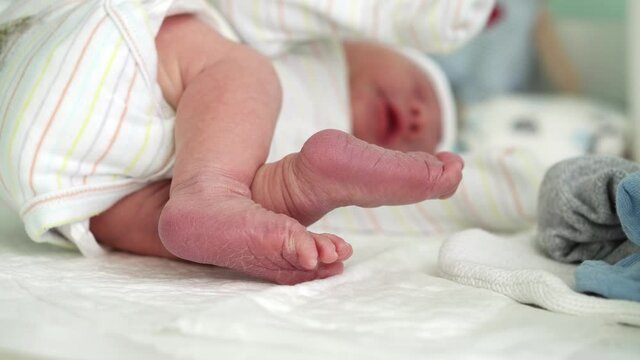 Tiny Cute Newborn Babies Bare Feet nd Toes First Days Of Life On White Background. Close up of Small Legs Dry Skin of Baby Infant. Mom changes diapers on changing table.Childhood, Maternity Concept.