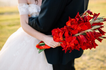 beautiful bouquet with red flowers in the hands of the bride. Newlyweds hug on a walk.