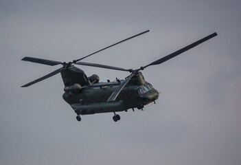 RAF Chinook tandem-rotor CH-47 helicopter flying fast and low in a cloudy blue grey sky on a...