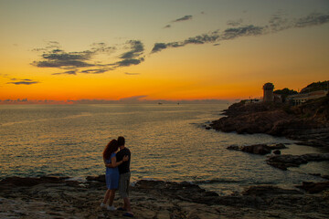 silhouettes of hugging man and woman on a mountain above the sea during sunset , in summer on vacation