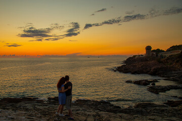 Fototapeta premium silhouettes of hugging man and woman on a mountain above the sea during sunset , in summer on vacation
