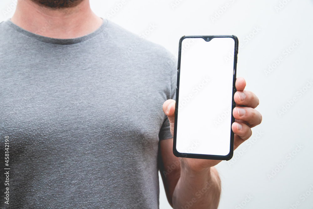 Wall mural View of a person weariang a grey t-shirt holding a smartphone in his hands on a white background