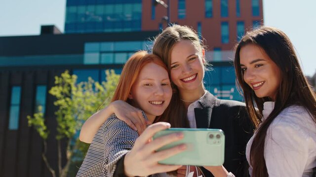 Beautiful with perfect smile ladies multiracial taking some pictures with smartphone beside of a modern architectural building