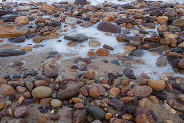soft blue waves coming through colourful pebbles at the beach in Adelaide, South Australia