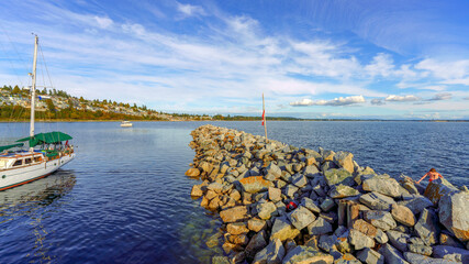 Fototapeta na wymiar Rock breakwater and private watercraft at Boundary Bay as seen from White Rock Pier on an end-of-summer afternoon, with views to White Rock water view residences