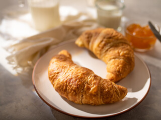 Traditional French style breakfast - two mouth-watering brown croissants, orange jam and fresh milk. Beautiful still life. Pastel shades. Restaurant, hotel, culinary blog, menu design.
