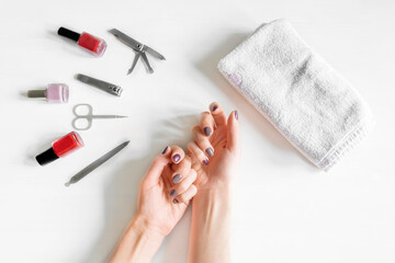 Obraz na płótnie Canvas Closeup of woman hands with polished nails and manicure instruments, bottles of nail polish. caucasian woman receiving french manicure at home or at nail salon. selfcare, beauty procedures yourself