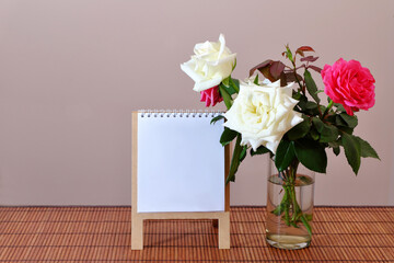 A bouquet of white and red roses in a glass on a bamboo tablecloth with a white sheet of paper on a stand