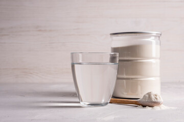 Collagen powder with a glass of water on a gray background with copy space.