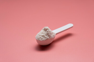 Fototapeta na wymiar White collagen powder on a plastic measure spoon on a pink background.