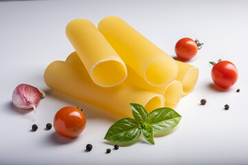 Raw cannelloni pasta on white background with cherry tomatoes, garlic and basil.