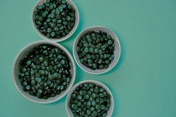 Spirulina algae dry tablets. Spirulina pills in cups on a green background. Vegetarian omega...