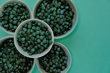 Spirulina algae dry tablets. Spirulina pills in cups on a green background. Vegetarian omega three.Omega three alternative source. Super food. 