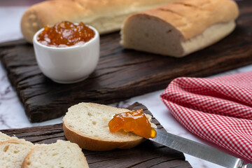 snack or breakfast with homemade sweet fruit jam in white bowl with slices of homemade bread on wooden board