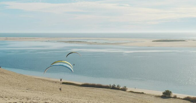 Paragliders In Dune Of Pilat With Scenic View Of Arcachon Bay During Summer In France. Wide Shot
