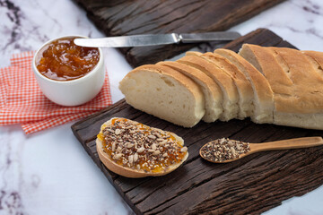 snack or breakfast with homemade sweet fruit jam in white bowl with slices of homemade bread on wooden board