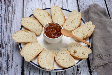homemade sweet fruit jam in white bowl with slices of homemade bread on white plate