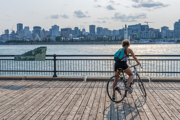 Obraz premium Montreal, Quebec, Canada - August 3 2021 : A woman rides a bicycle and watching the sunset in Jean-Drapeau park maritime shuttle landing stage. Saint Helens Island.