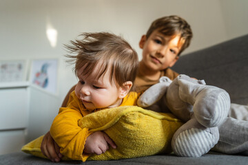 Small caucasian boy five years old lying on the bed with his baby brother or sister playing in bright room real people family bonding siblings brother and sister