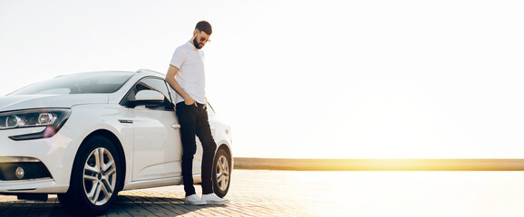 Handsome bearded man in sunglasses stands near his modern white car, smiling business man near the...